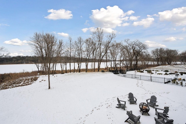 snowy yard with a fire pit, a water view, and fence