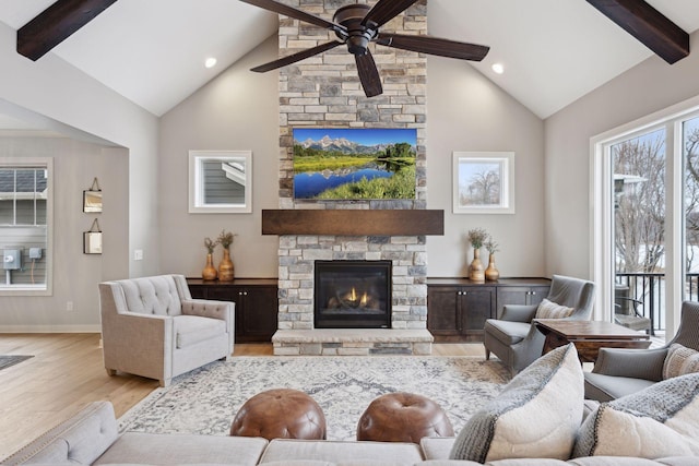 living area with baseboards, beamed ceiling, a stone fireplace, wood finished floors, and a ceiling fan