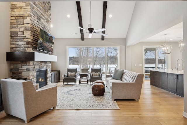 living area featuring ceiling fan with notable chandelier, high vaulted ceiling, a stone fireplace, and light wood finished floors