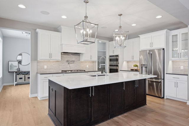 kitchen with stainless steel appliances, light wood-style floors, an island with sink, and white cabinetry