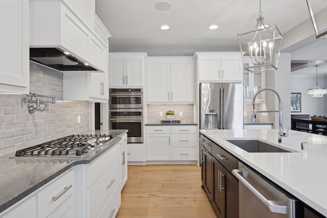 kitchen with a chandelier, decorative light fixtures, appliances with stainless steel finishes, white cabinets, and a sink