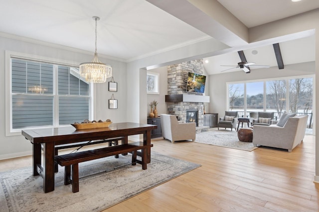 dining area featuring light wood-type flooring, ceiling fan with notable chandelier, a fireplace, baseboards, and vaulted ceiling with beams