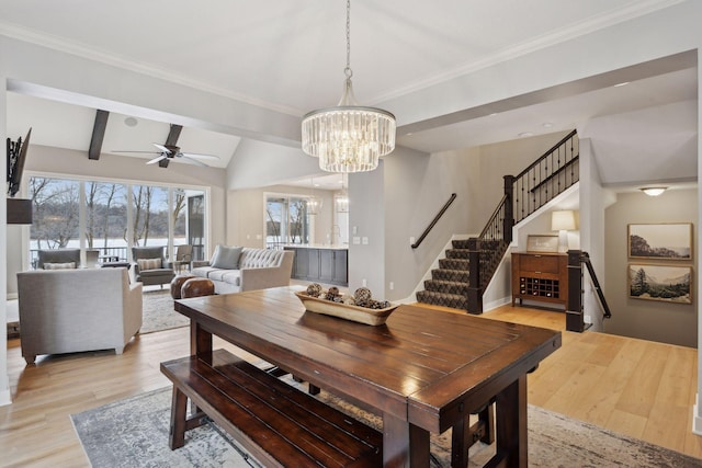 dining space with stairs, lofted ceiling with beams, ornamental molding, ceiling fan with notable chandelier, and light wood-style floors