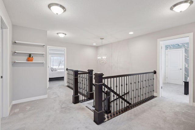 hall with an upstairs landing, a textured ceiling, carpet floors, baseboards, and a chandelier