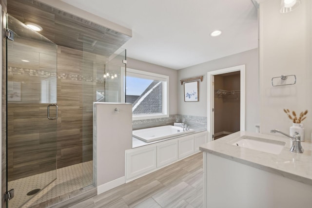 bathroom with a stall shower, vanity, a walk in closet, and a garden tub