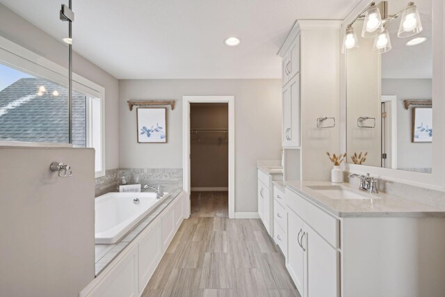 bathroom with a bath, a spacious closet, vanity, and baseboards