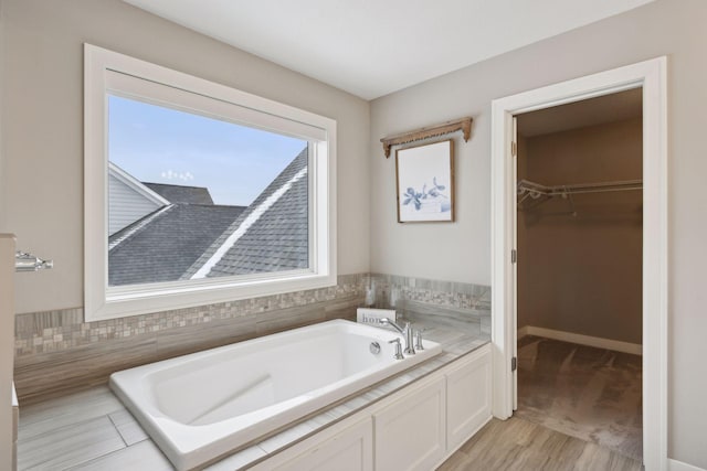 bathroom featuring a garden tub, a spacious closet, and baseboards