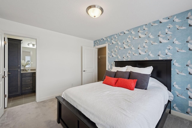 bedroom featuring a spacious closet, wallpapered walls, baseboards, light carpet, and ensuite bath