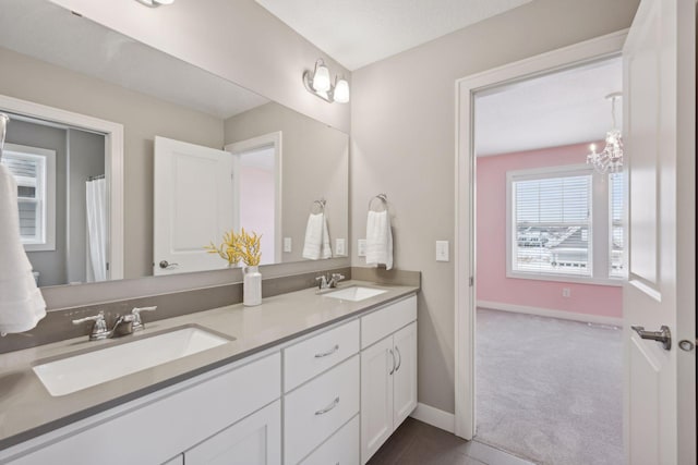 bathroom featuring a sink, baseboards, an inviting chandelier, and double vanity