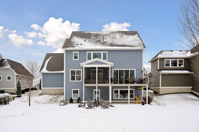 snow covered house with a patio, a wooden deck, a sunroom, and an outdoor fire pit