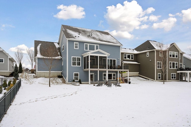 snow covered back of property featuring fence and a sunroom