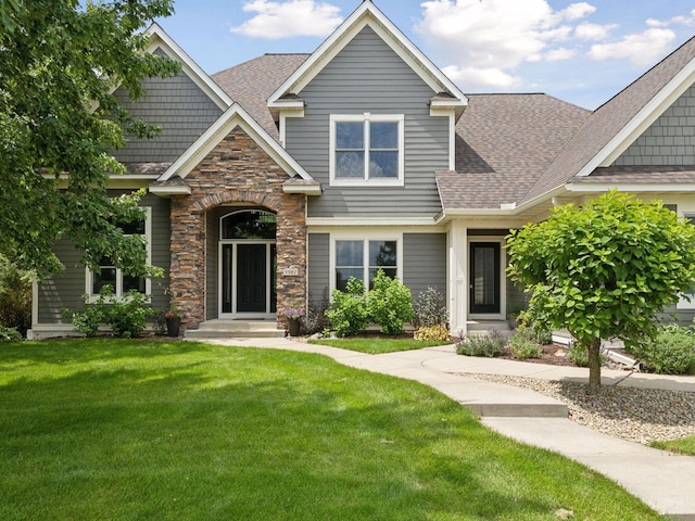 craftsman-style house featuring a front yard, stone siding, and a shingled roof