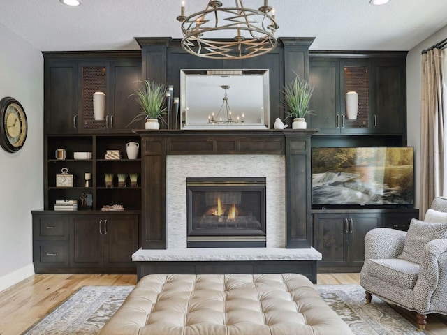 living room featuring a glass covered fireplace, an inviting chandelier, light wood-style flooring, and a textured ceiling