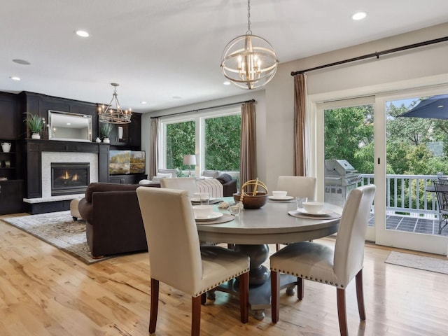 dining area featuring recessed lighting, light wood-style floors, a notable chandelier, and a glass covered fireplace