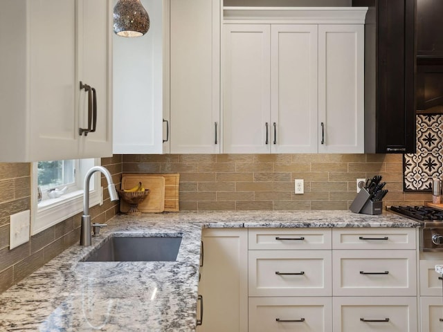 kitchen featuring white cabinetry, light stone countertops, backsplash, and a sink