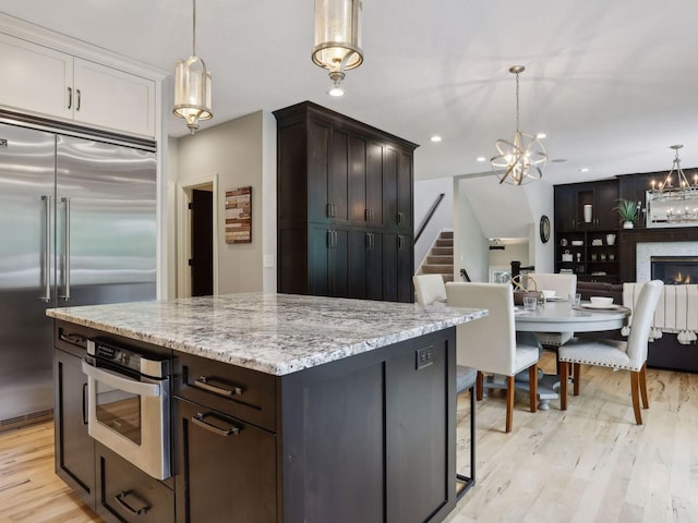 kitchen featuring light wood finished floors, decorative light fixtures, light stone counters, an inviting chandelier, and stainless steel appliances