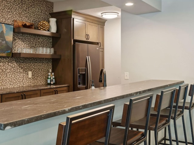 kitchen with decorative backsplash, open shelves, a kitchen breakfast bar, and stainless steel fridge with ice dispenser