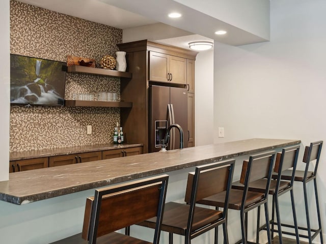 kitchen with dark countertops, stainless steel fridge with ice dispenser, a breakfast bar, decorative backsplash, and open shelves