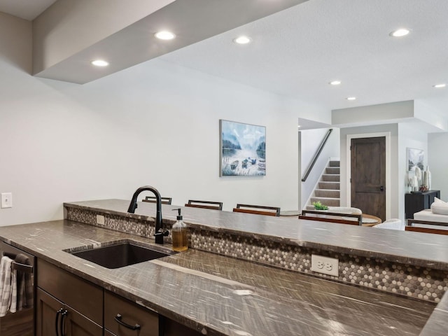 kitchen featuring dark brown cabinetry, dishwasher, dark stone counters, recessed lighting, and a sink