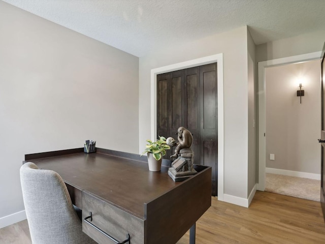 office space featuring baseboards, light wood-type flooring, and a textured ceiling