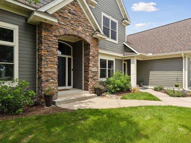 entrance to property with stone siding, a lawn, and roof with shingles