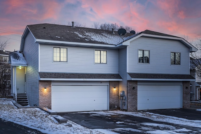 traditional-style home with an attached garage, driveway, roof with shingles, and brick siding