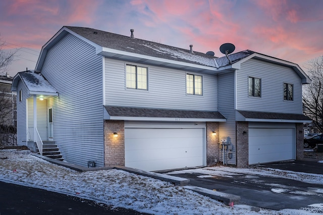 view of front of home featuring an attached garage, driveway, a shingled roof, and brick siding