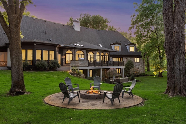 back house at dusk with a patio, a balcony, a yard, and an outdoor fire pit