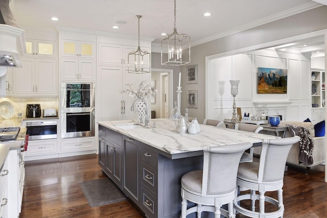 kitchen featuring appliances with stainless steel finishes, a kitchen island with sink, ornamental molding, white cabinets, and decorative light fixtures