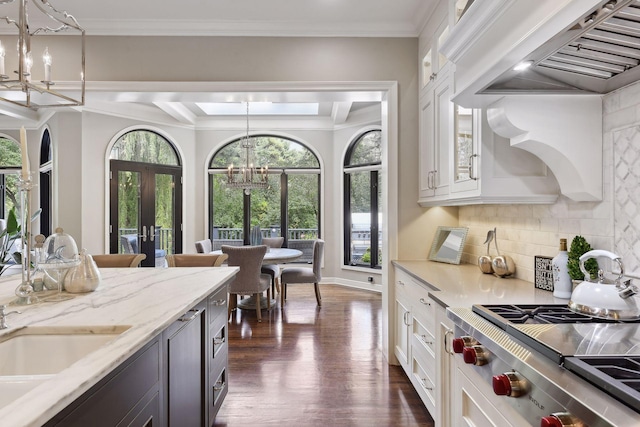 kitchen with white cabinetry, light stone countertops, custom range hood, decorative light fixtures, and a chandelier