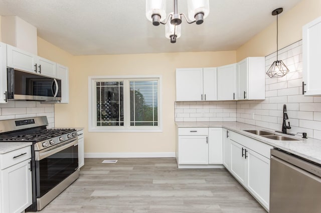 kitchen featuring appliances with stainless steel finishes, white cabinets, and decorative light fixtures