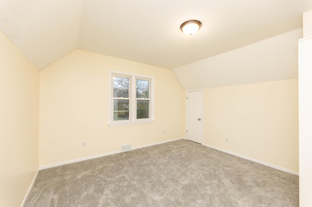 bonus room with lofted ceiling, light colored carpet, and a textured ceiling