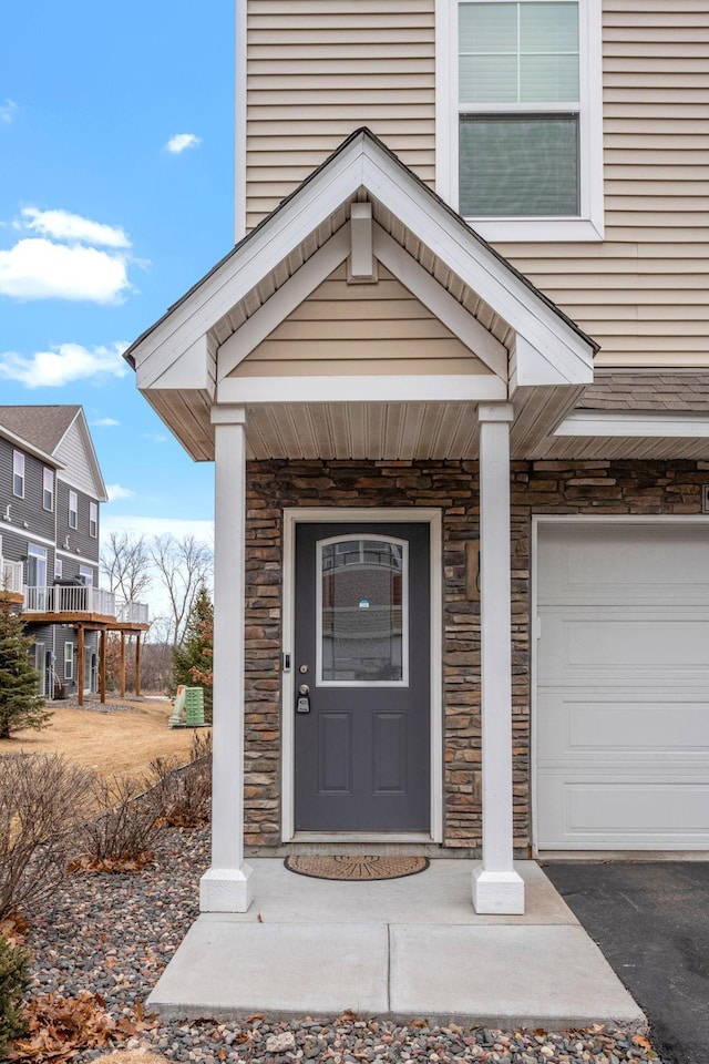 view of exterior entry featuring a garage, stone siding, driveway, and a porch