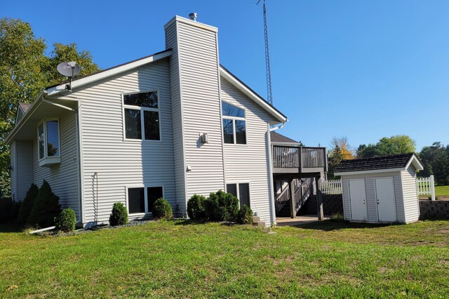 rear view of property with a wooden deck, a lawn, and a storage shed