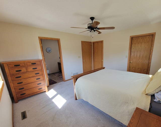 bedroom with light carpet, ceiling fan, and ensuite bath