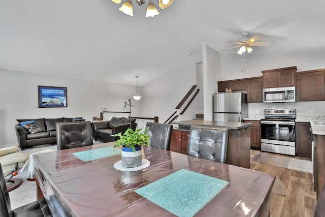 dining area with ceiling fan with notable chandelier, vaulted ceiling, and wood-type flooring