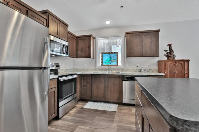 kitchen with sink, stainless steel appliances, dark brown cabinets, a textured ceiling, and light hardwood / wood-style flooring