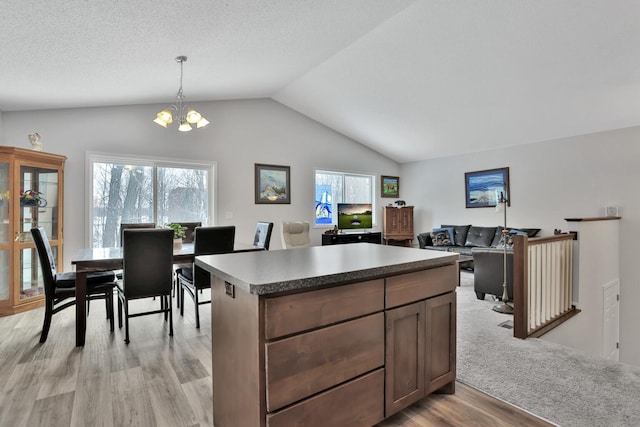 kitchen with vaulted ceiling, pendant lighting, a center island, light hardwood / wood-style floors, and an inviting chandelier