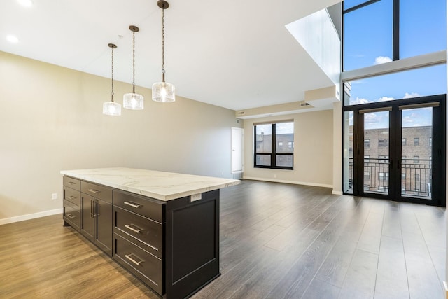 kitchen featuring decorative light fixtures, dark brown cabinets, dark hardwood / wood-style flooring, a kitchen island, and light stone countertops