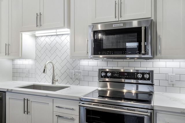 kitchen featuring white cabinetry, sink, light stone counters, and appliances with stainless steel finishes