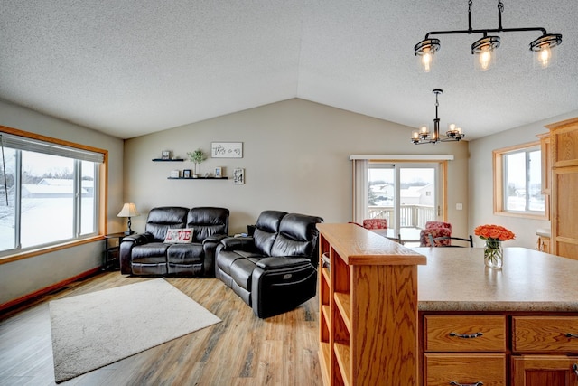 living area with a textured ceiling, light wood-type flooring, lofted ceiling, and an inviting chandelier