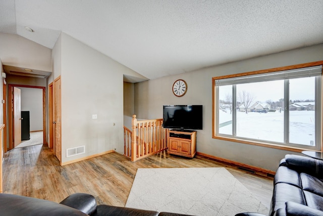 living area featuring lofted ceiling, light wood-style floors, visible vents, and baseboards