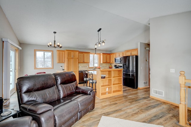 living area with an inviting chandelier, visible vents, light wood finished floors, and vaulted ceiling