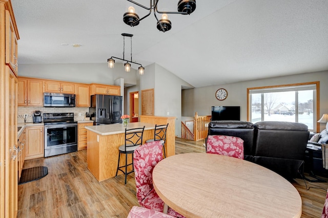 interior space with a center island, vaulted ceiling, appliances with stainless steel finishes, light hardwood / wood-style floors, and backsplash