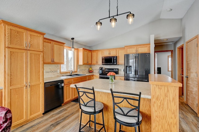 kitchen featuring sink, a center island, hanging light fixtures, light wood-type flooring, and black appliances