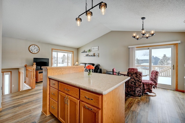 kitchen with a center island, light hardwood / wood-style floors, a textured ceiling, decorative light fixtures, and vaulted ceiling