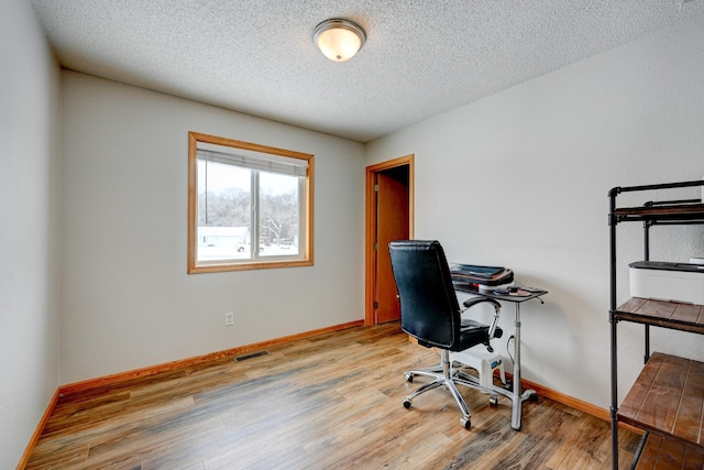 home office with a textured ceiling, wood finished floors, visible vents, and baseboards