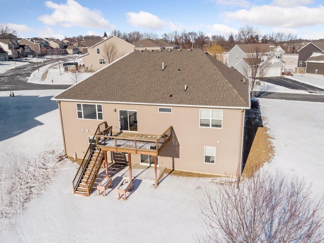 snow covered back of property featuring a shingled roof, stairs, a residential view, and a deck