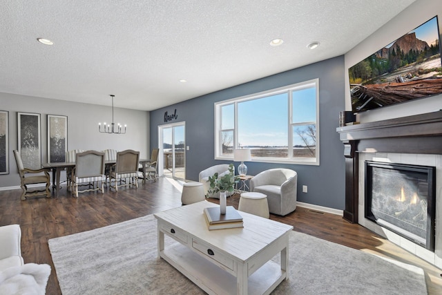 living area with a notable chandelier, dark wood finished floors, a glass covered fireplace, a textured ceiling, and baseboards