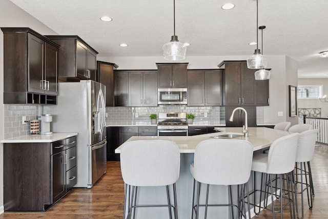 kitchen with stainless steel appliances, a sink, light countertops, a center island with sink, and pendant lighting